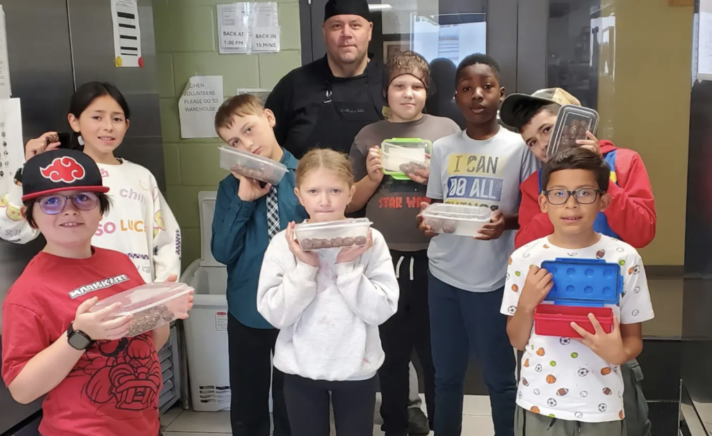 Children and their instructor hold containers of food prepared during a cooking class.