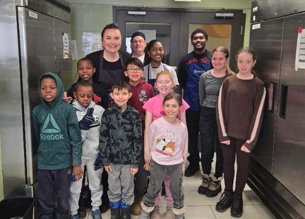 Children and adult instructors pose together inside a commercial kitchen.