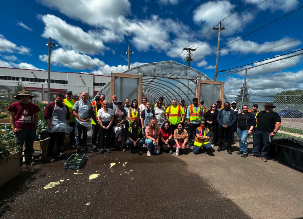 Community members and volunteers gathered in front of a garden greenhouse