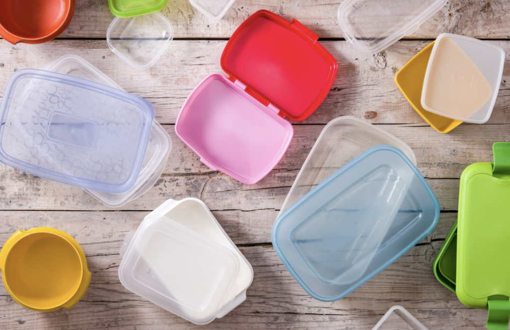 Assorted reusable plastic food containers and colourful lids on a wooden surface.